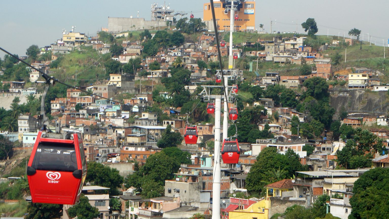 Cabines vermelhas do teleférico passam sobre as casas do morro